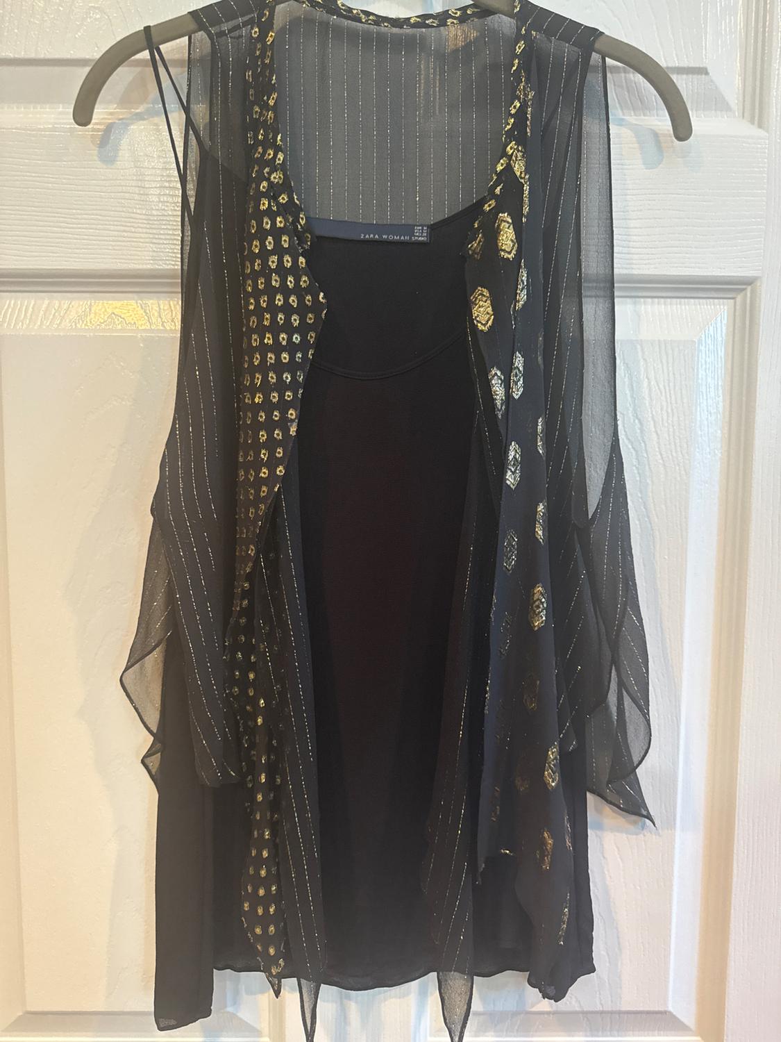 Semi-sheer black waistcoat with a gold print and silver stripes, hanging on a hanger in front of a white door.