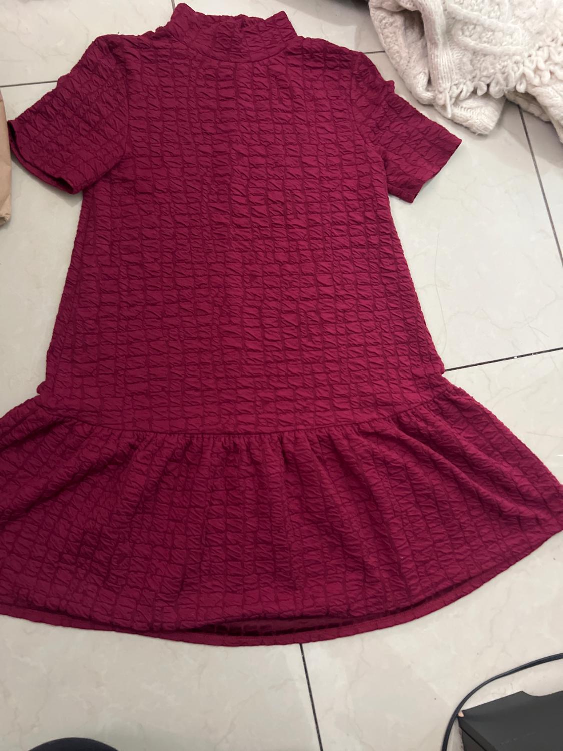 Textured red short-sleeved roll-neck dress, spread out on a light-coloured floor, with white fabric in the background.