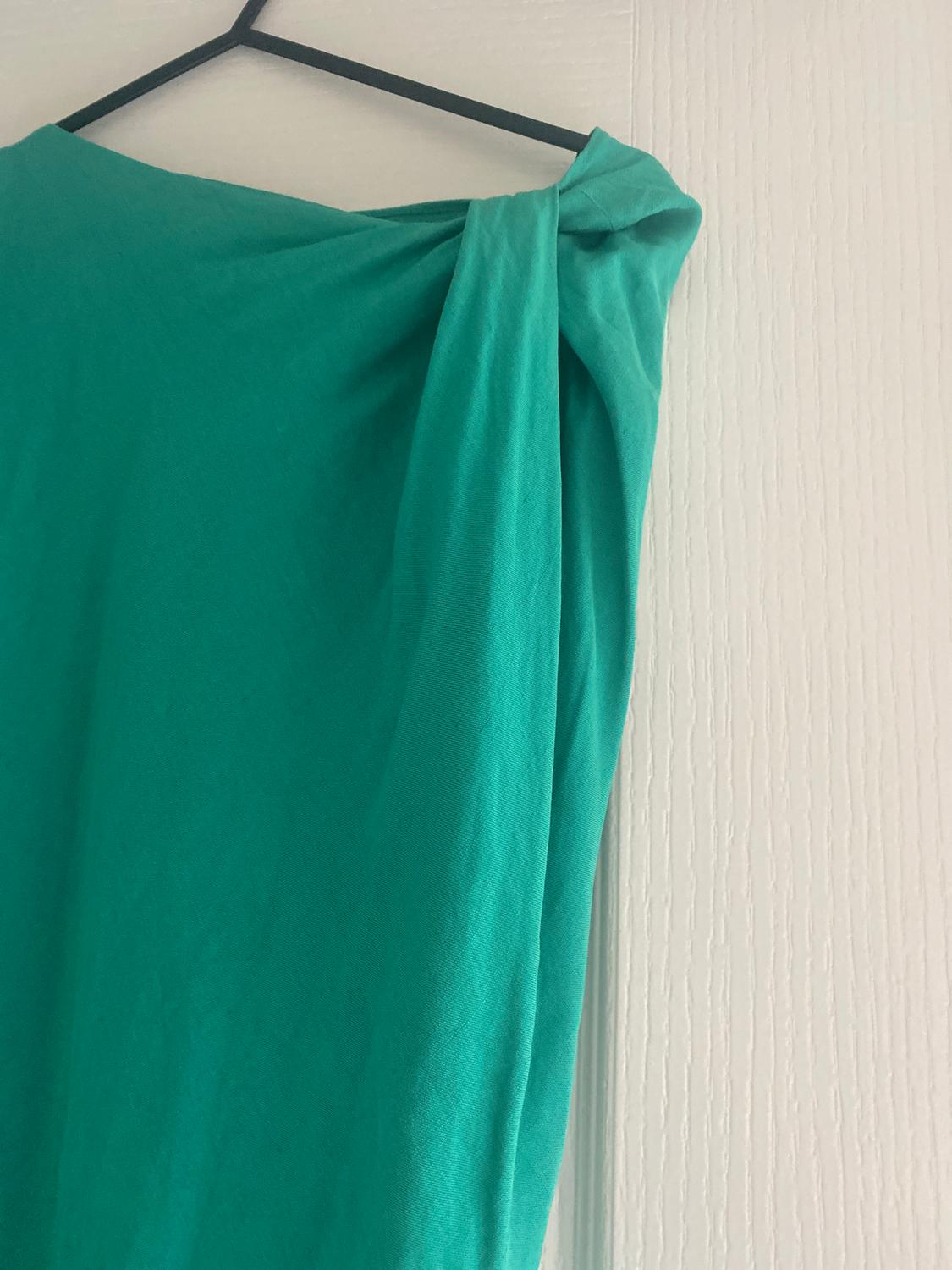 Green draped fabric hung on a black hanger against a textured white wall.