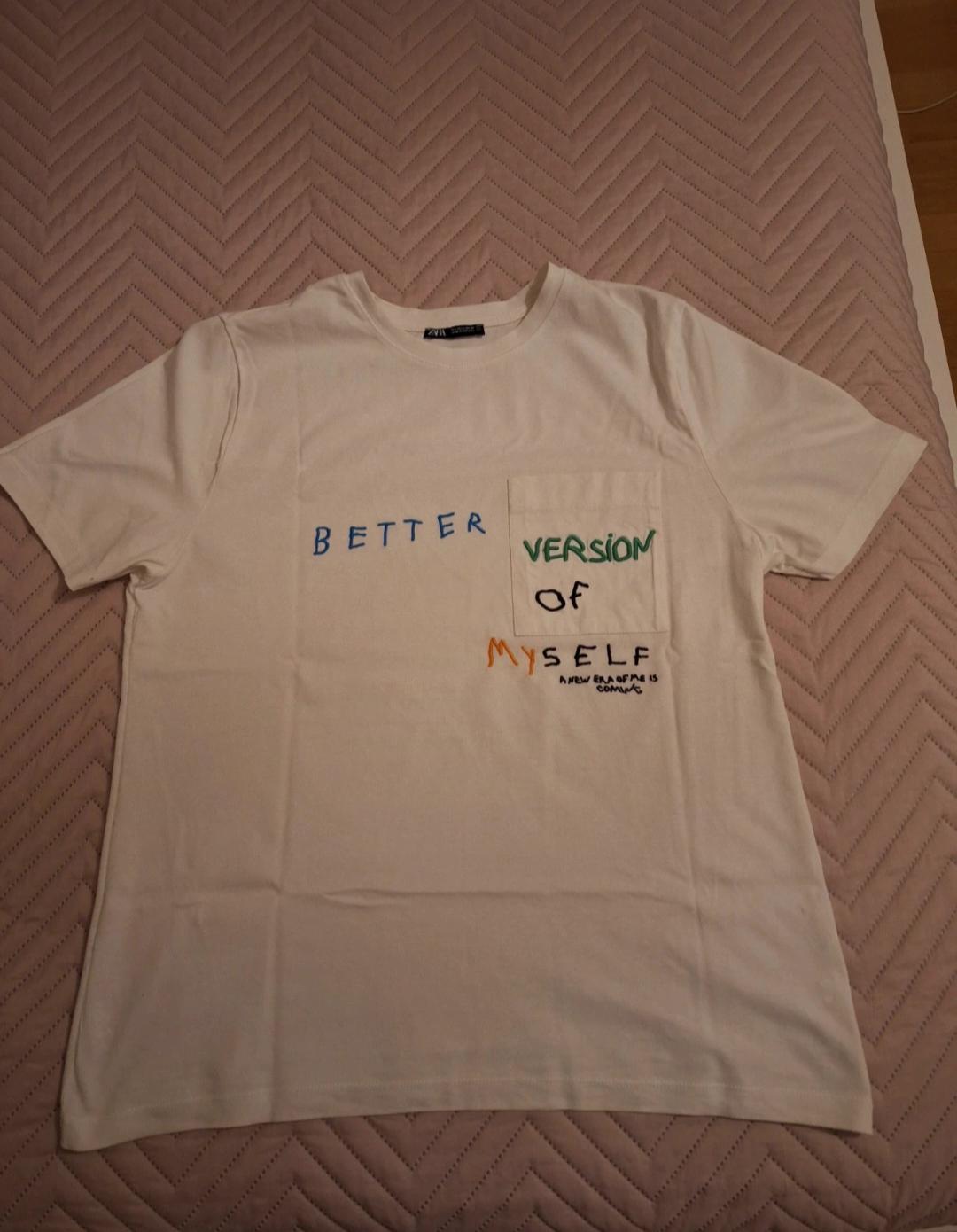White T-shirt with colourful text: "BETTER VERSION OF MYSELF" on a bed with a pink herringbone patterned bedspread.
