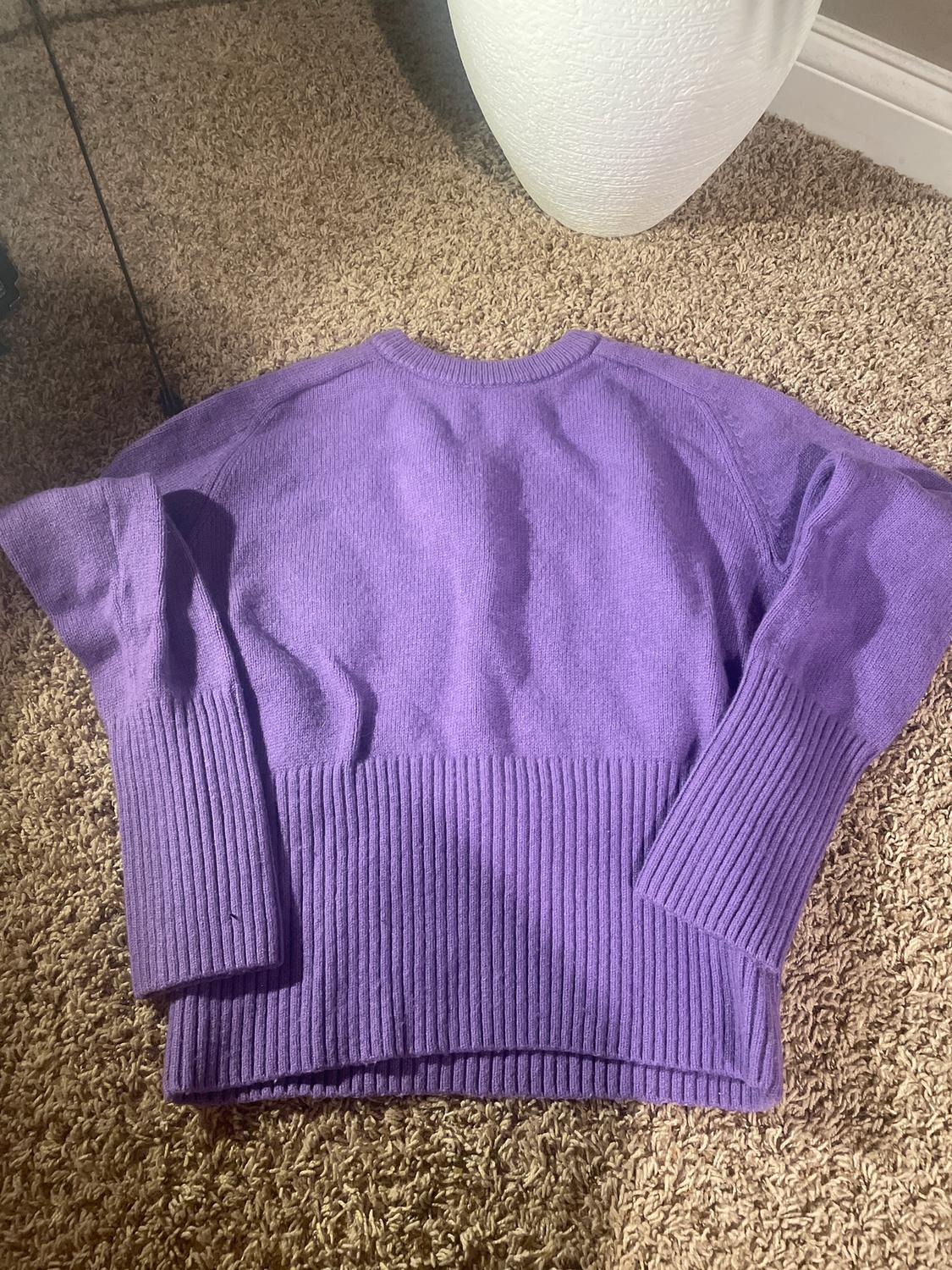 Purple chunky knit jumper with long sleeves, placed on a beige rug next to a white vase.