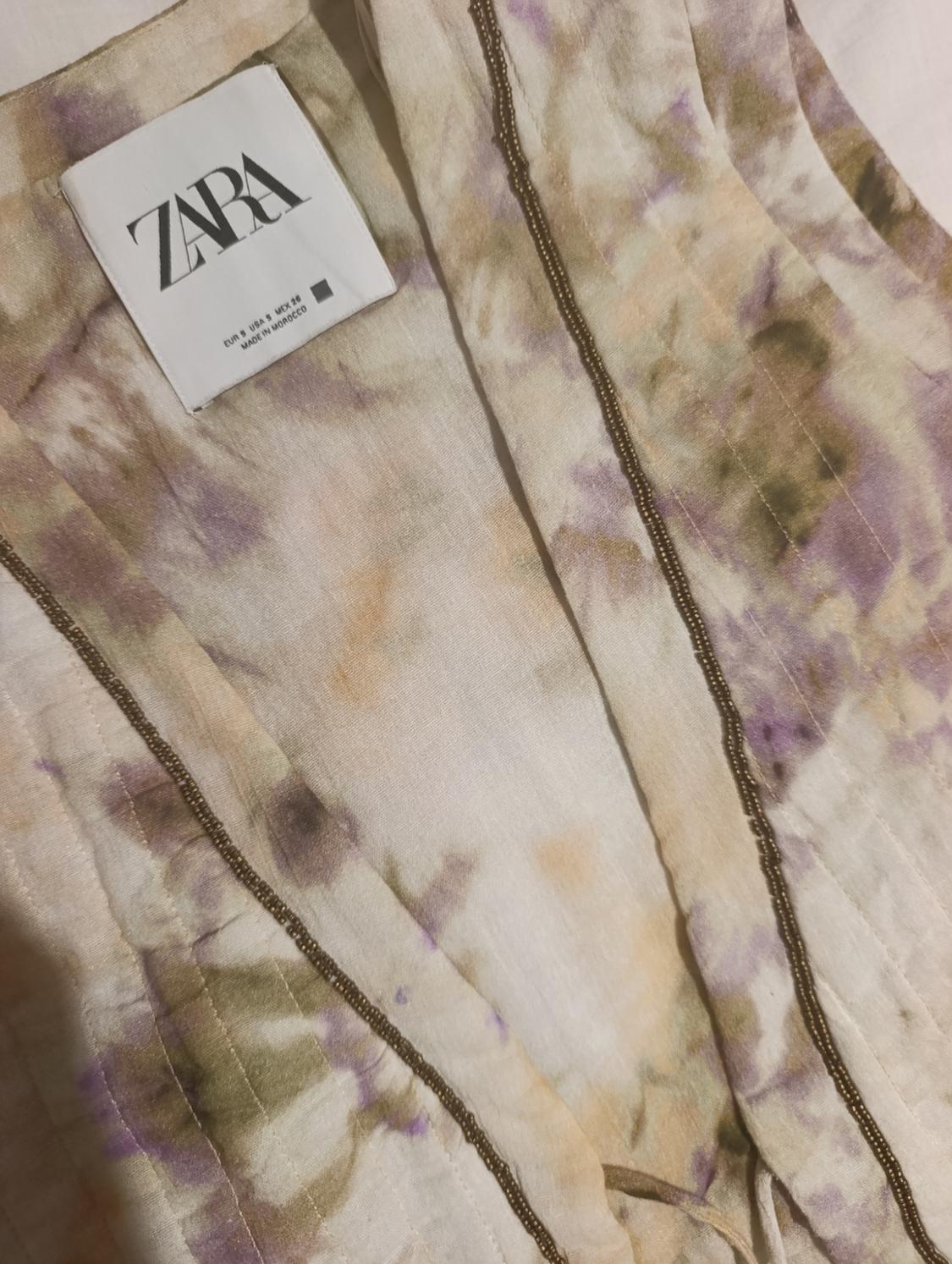 Zara label on fabric with a print in beige, purple, and green tones. Visible text: "ZARA" and "MADE IN MOROCCO".
