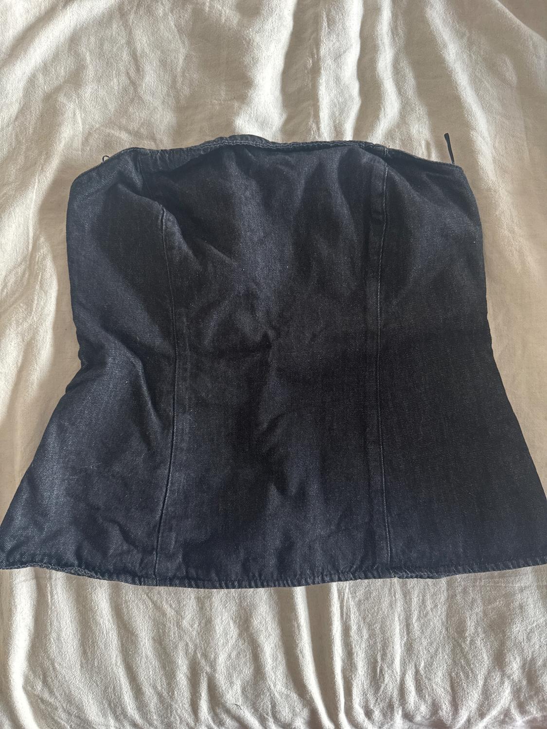 Black strapless denim top on a beige fabric surface with visible creases.