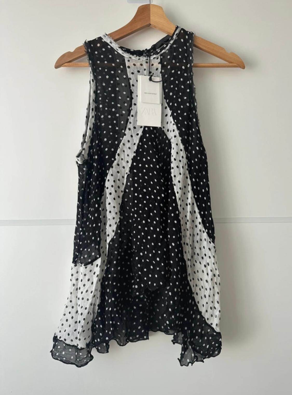 Black and white polka dot sleeveless blouse hanging on a wooden hanger. Visible label with text "ZARA".