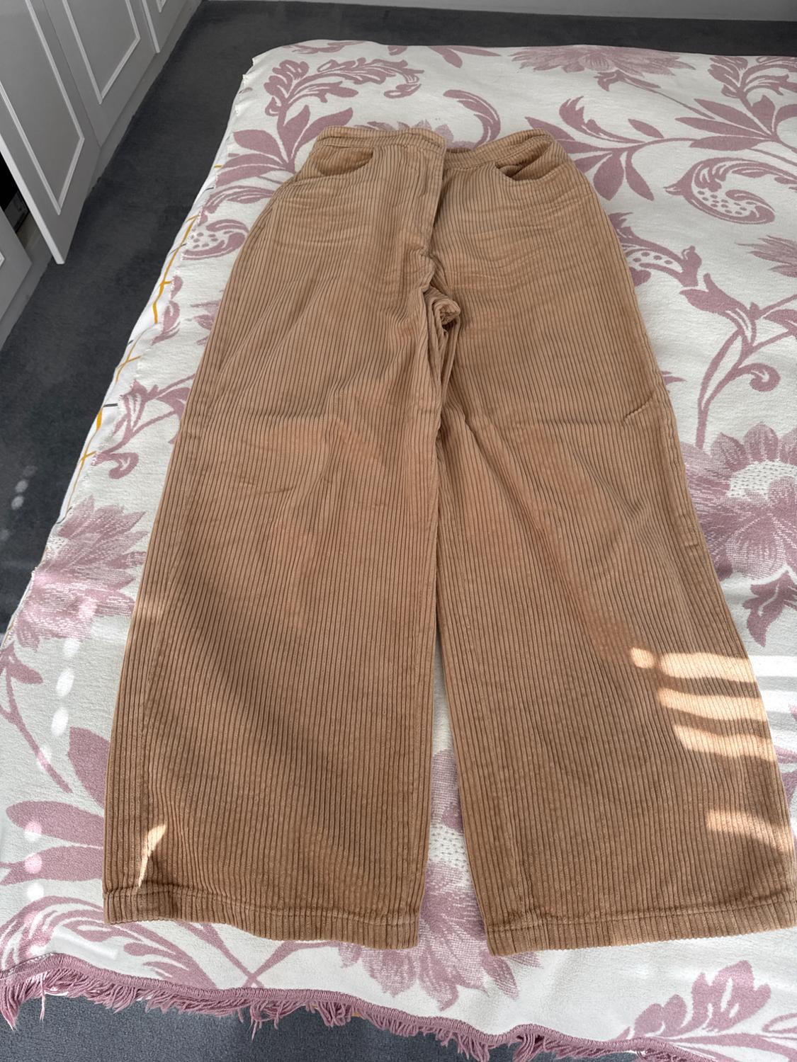 Light brown corduroy trousers with pockets, placed on a bed with a pink and white floral bedspread.