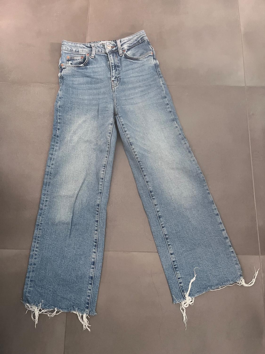 Light blue denim jeans with a frayed hem, placed on a grey background.