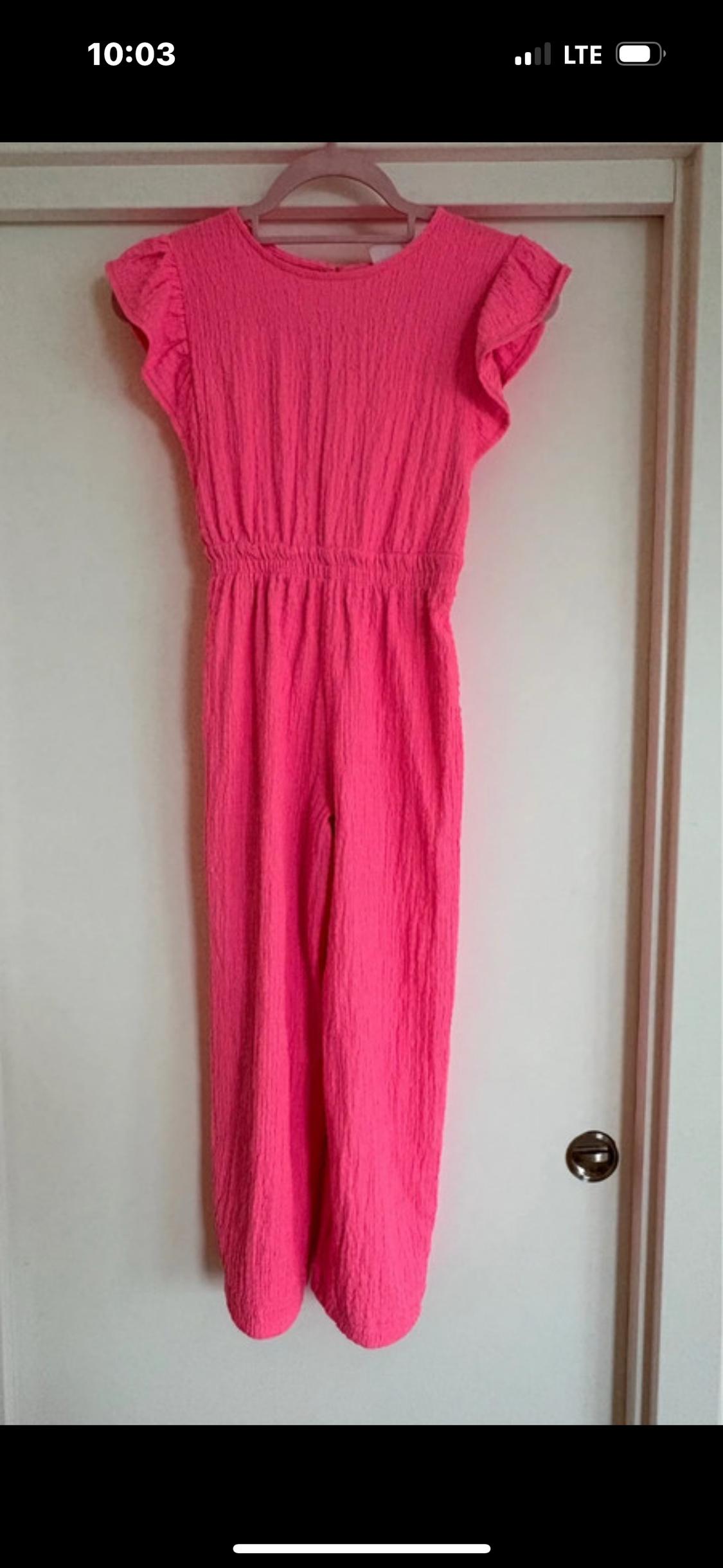 Textured pink jumpsuit hanging on a hanger over a white door. Short frill sleeves and elasticated waist.