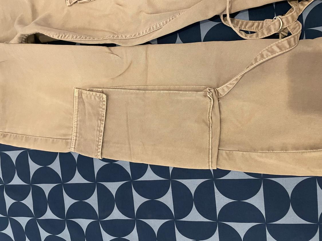 Beige trousers with a large pocket and belt, on a blue fabric background with a circular geometric pattern.