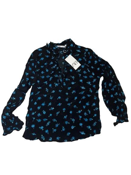 Black blouse with blue floral print and white hang tag with black lettering. Long sleeves and frilled collar.