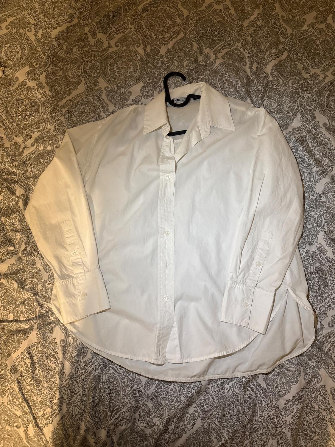 White long-sleeved shirt on a hanger, placed on a bedspread with a grey and white pattern design.
