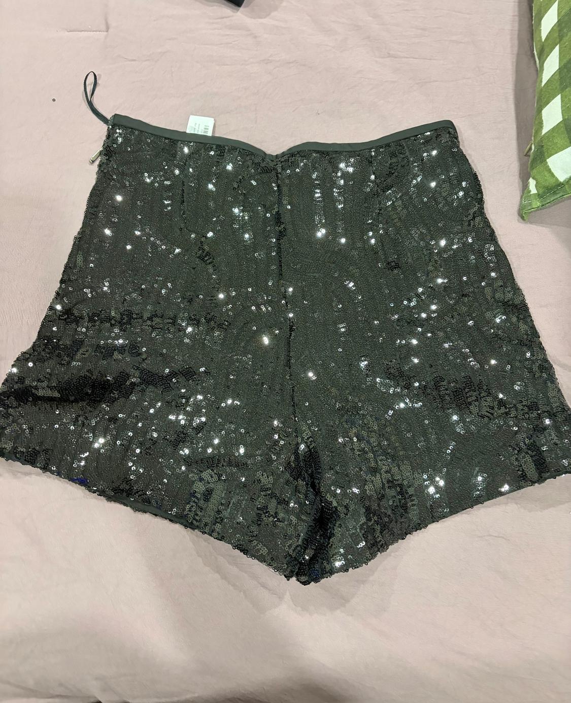 Black shorts with sparkly sequins on a light surface. Label visible at the top.