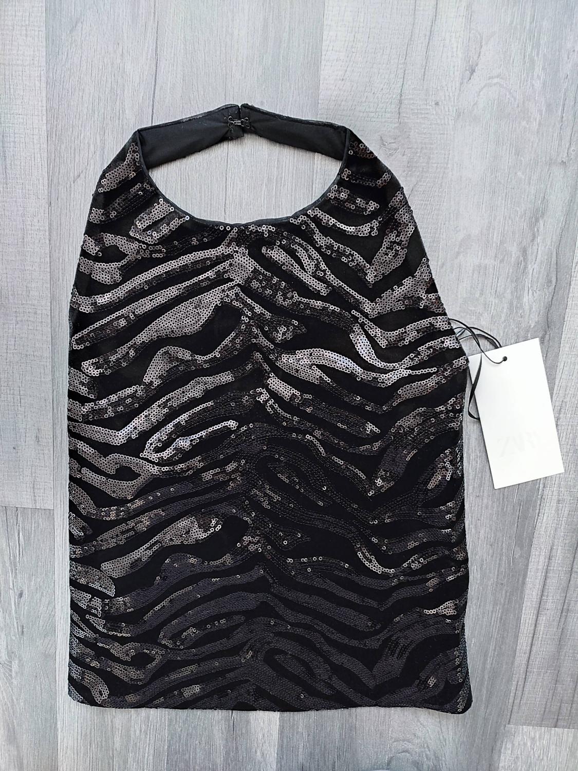 Black halter-neck top with silver sequin zebra print on a grey wooden background. White label with the text ZARA.