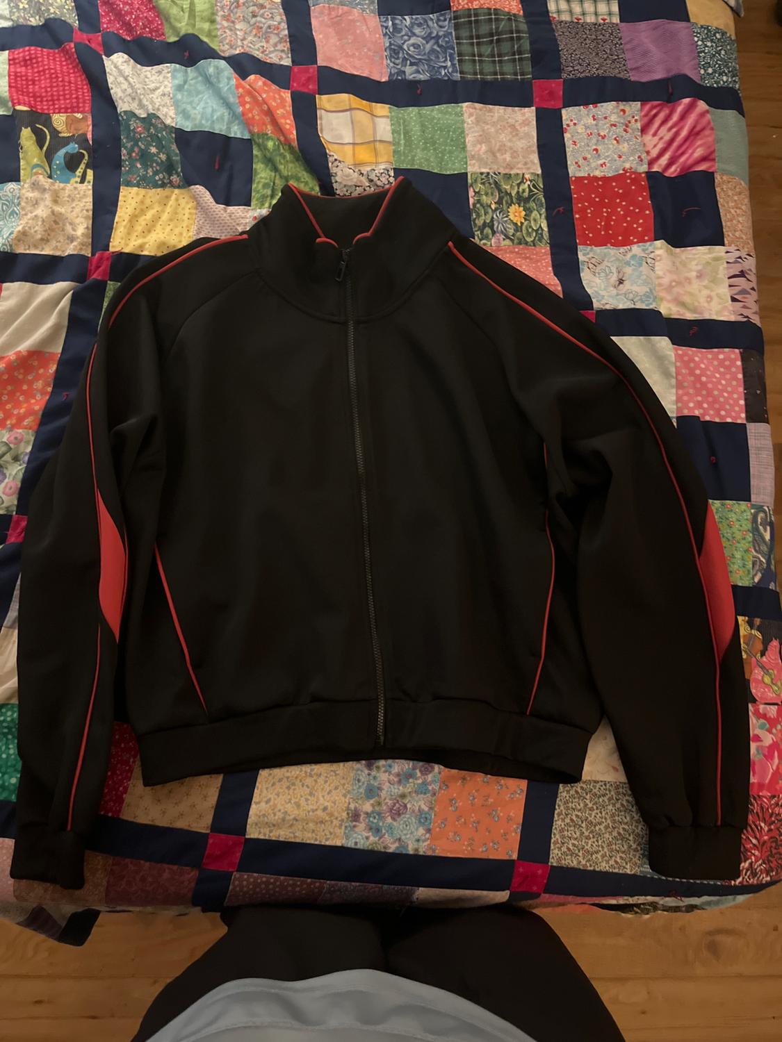Black jacket with red details on a colourful patchwork quilt. The jacket has a zip and a high collar.
