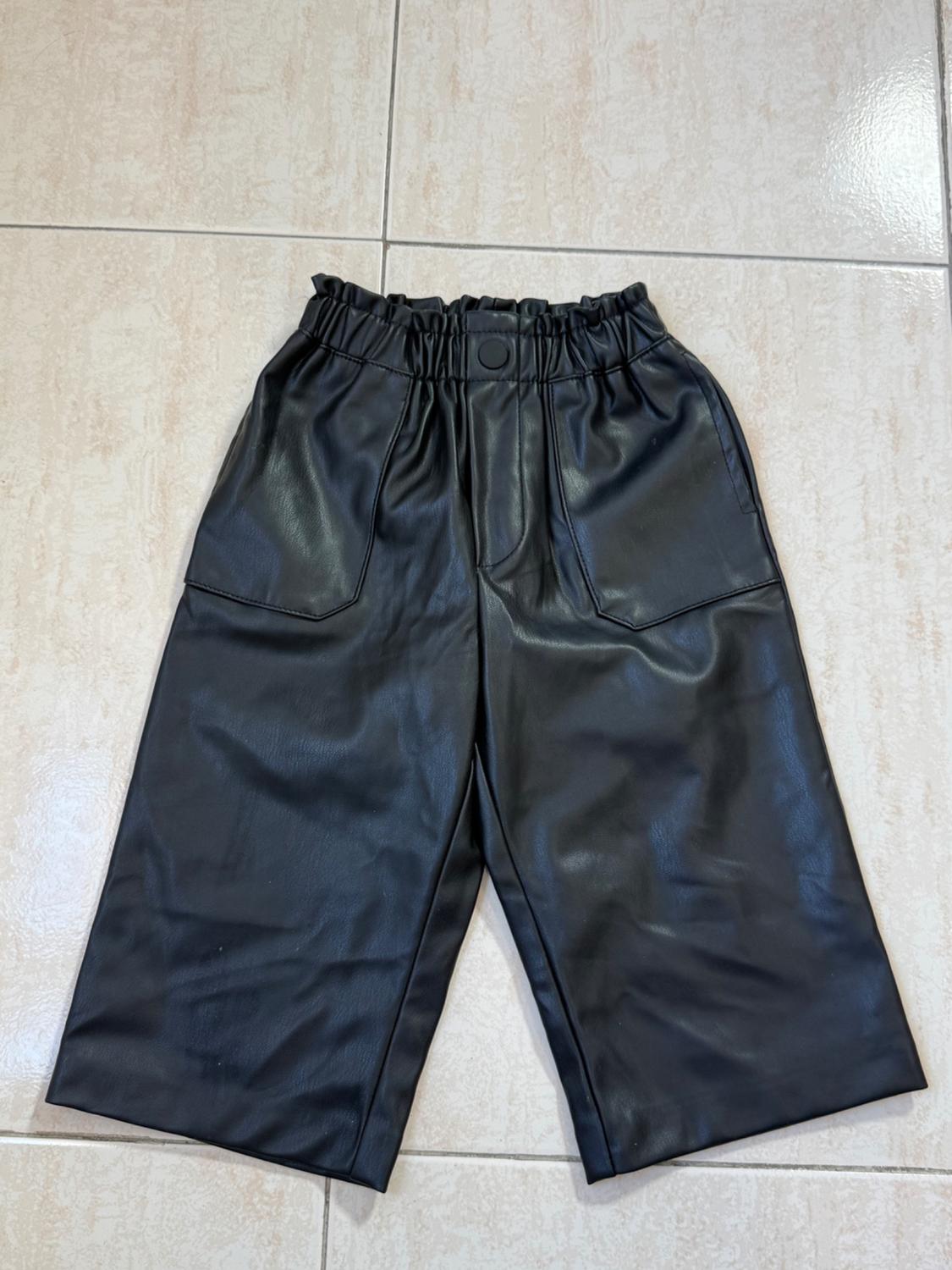 Black leather shorts with an elasticated waistband and large pockets, laid out on a light tiled floor.