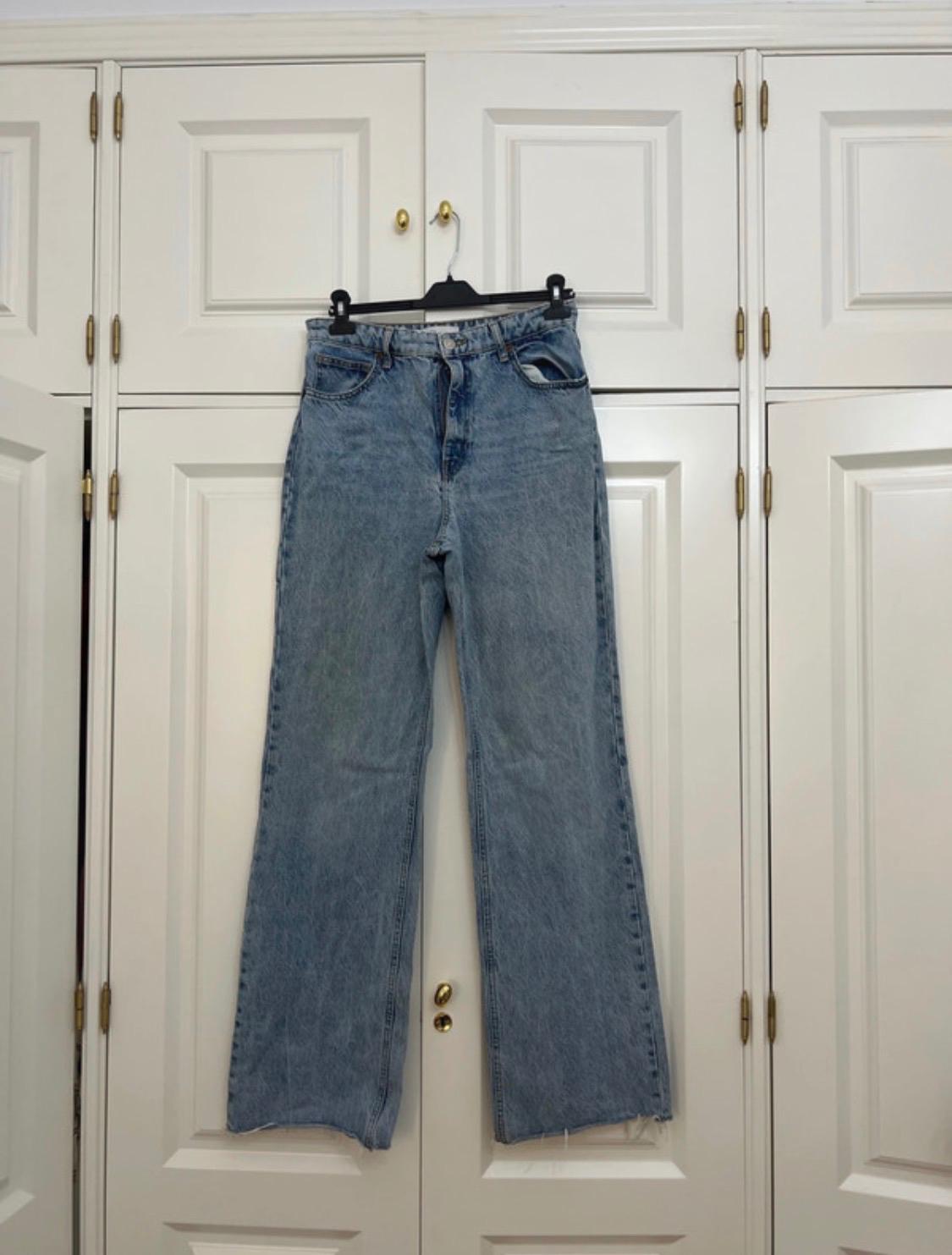 Light blue wide-leg jeans with a frayed hem, hanging on a black hanger in front of a classic white wardrobe.