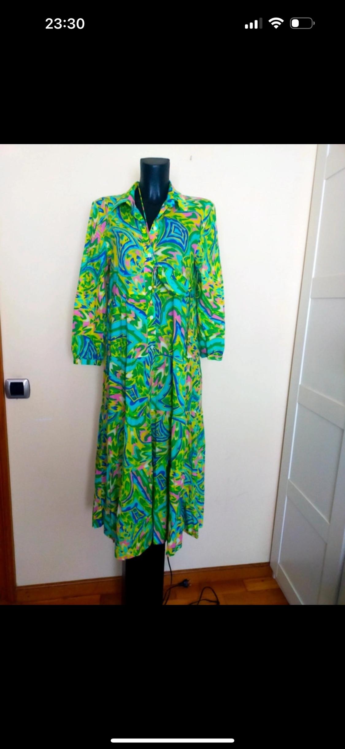 Long dress with psychedelic print in green, blue and pink on a black mannequin in a room with wooden floor.