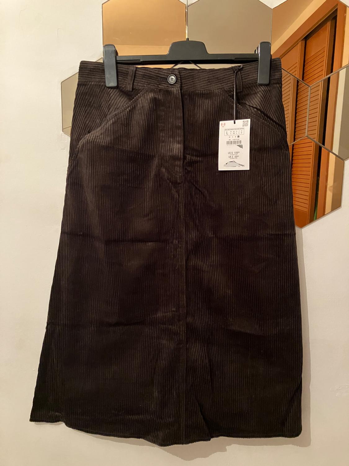 Brown corduroy skirt hanging on a black hanger, with visible price tag. Background with hexagonal mirror.