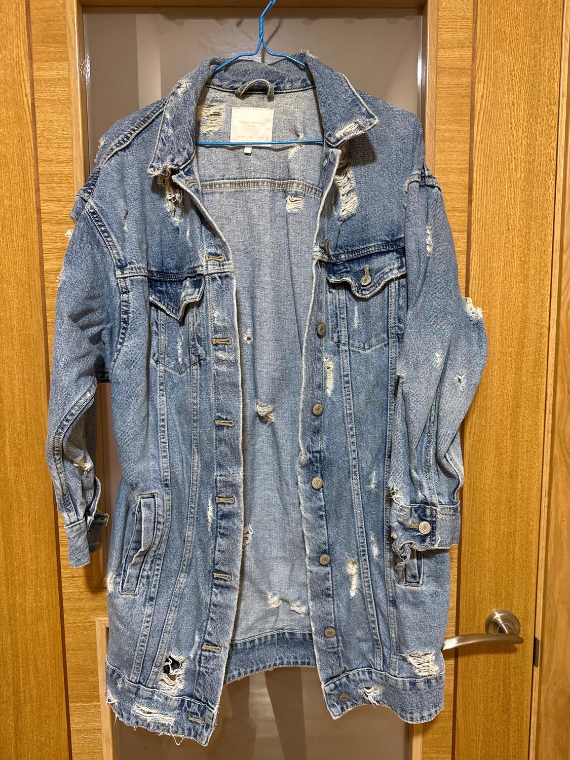 Worn blue denim jacket hanging on a blue hanger over a light wooden door.