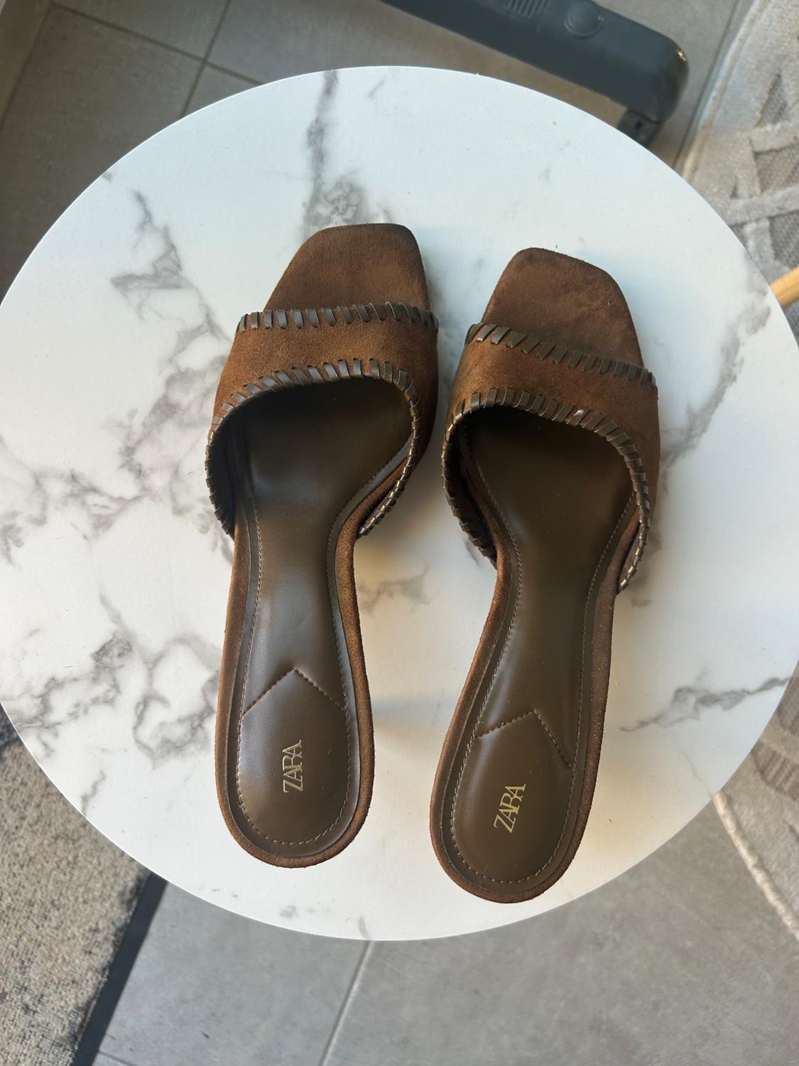 Brown heeled slingback sandals on a white marble table. The text ZARA can be read on the insole.