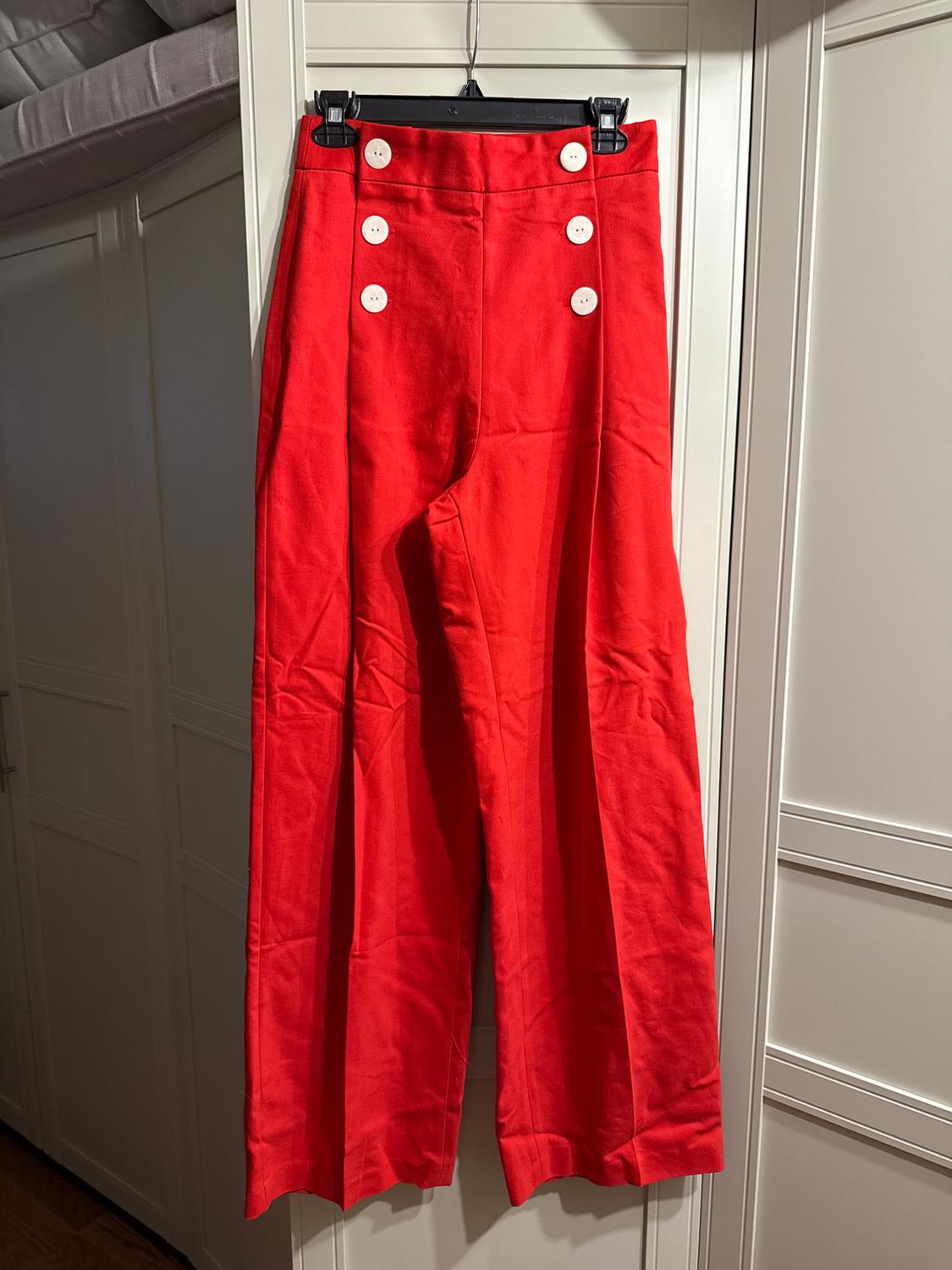Red wide-leg pants with six white buttons on the front, hanging on a black hanger in front of a closet.