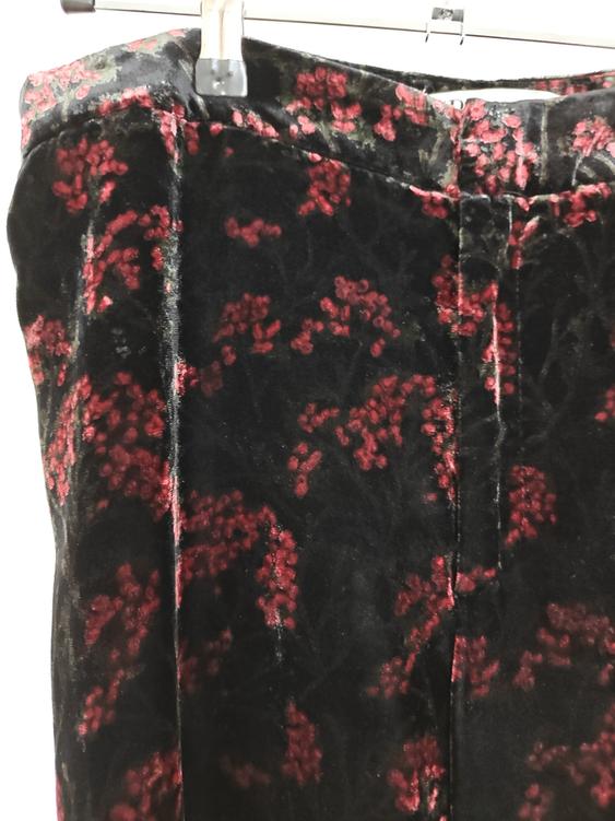 Black velvet trousers with a red floral print, hanging on a hanger. White background.