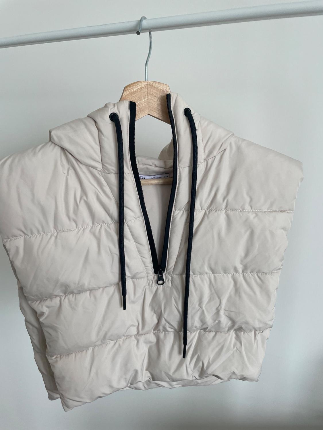 Front view of beige padded gilet with hood and black drawstrings.