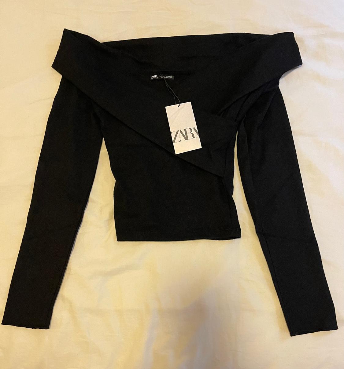 Black long-sleeved top with a wide neckline on a light surface. Visible label with the text "ZARA".