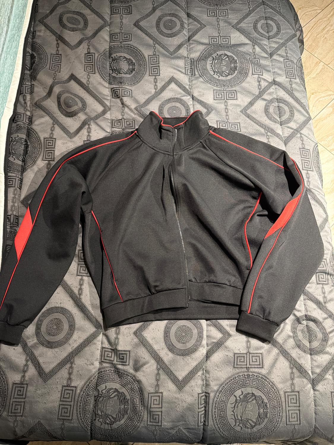 Black jacket with red details on a grey bedspread with geometric and lion patterns.