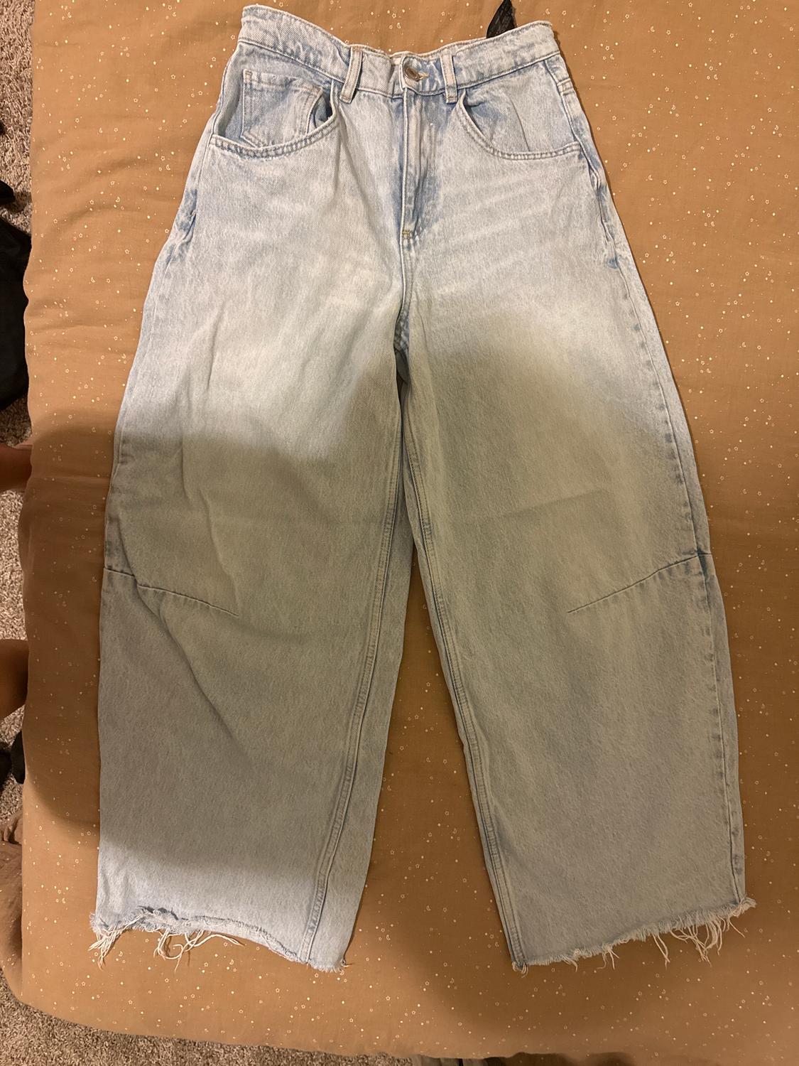 Wide-leg light denim jeans with a frayed hem, placed on a brown quilt with gold dots.