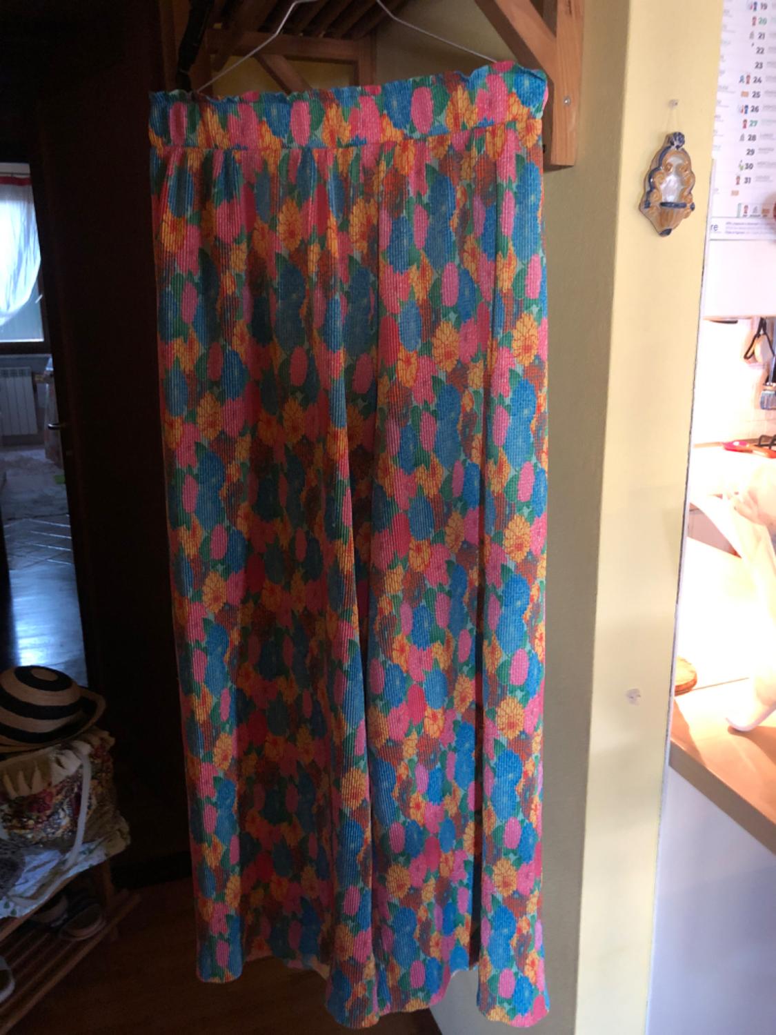 Long skirt with floral print in shades of blue, pink and yellow, hanging on a wooden hanger in an indoor setting.