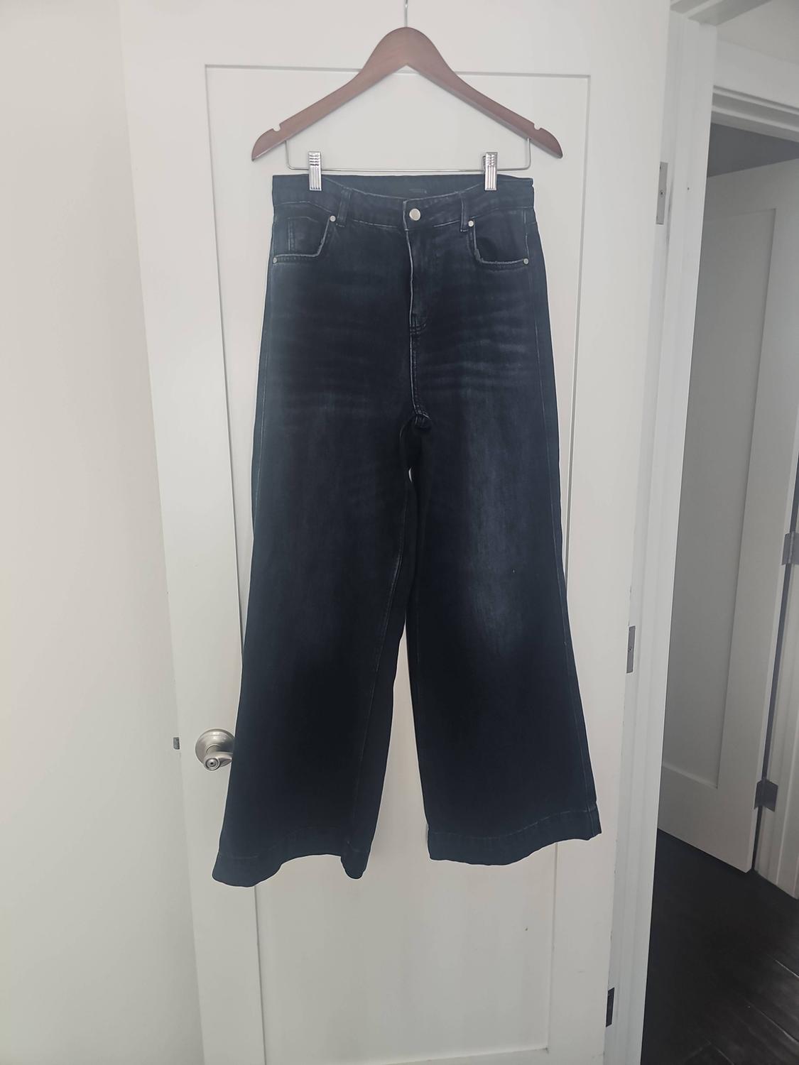 Dark blue wide-leg jeans hanging from clips on a wooden hanger over a white door.