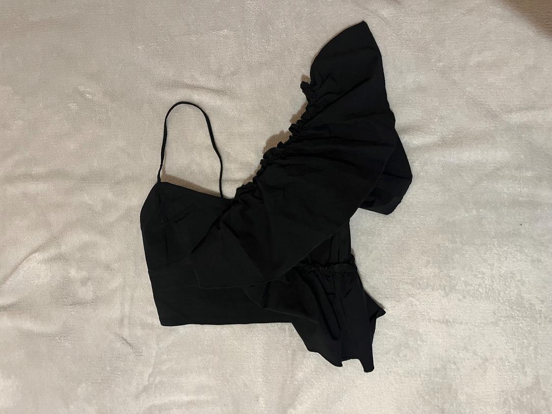 Black one-shoulder camisole top with ruffled sleeve, on a light surface.