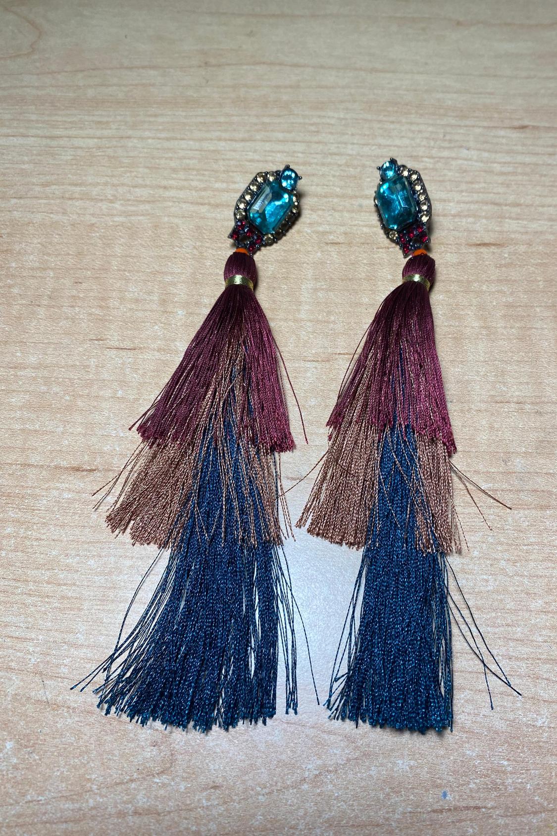 Front view of fringed earrings in burgundy, brown and blue shades, adorned with blue stones.