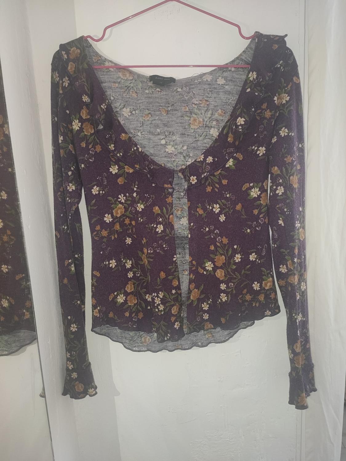Long-sleeved cardigan with a floral print in brown and beige tones on a purple background, hanging on a pink hanger.
