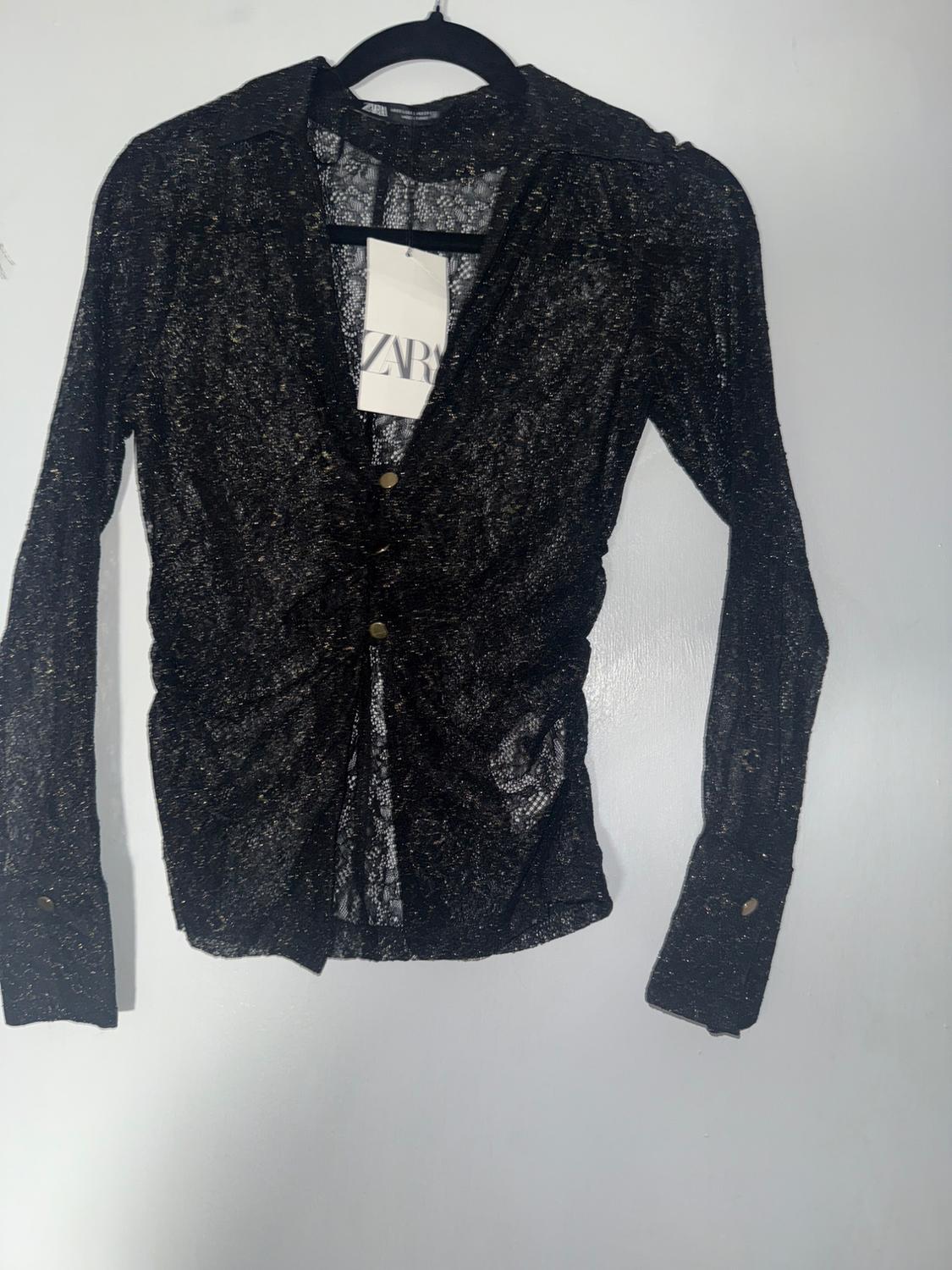 Black lace shirt hanging on a hanger, with a visible tag that says "ZARA", on a white background.