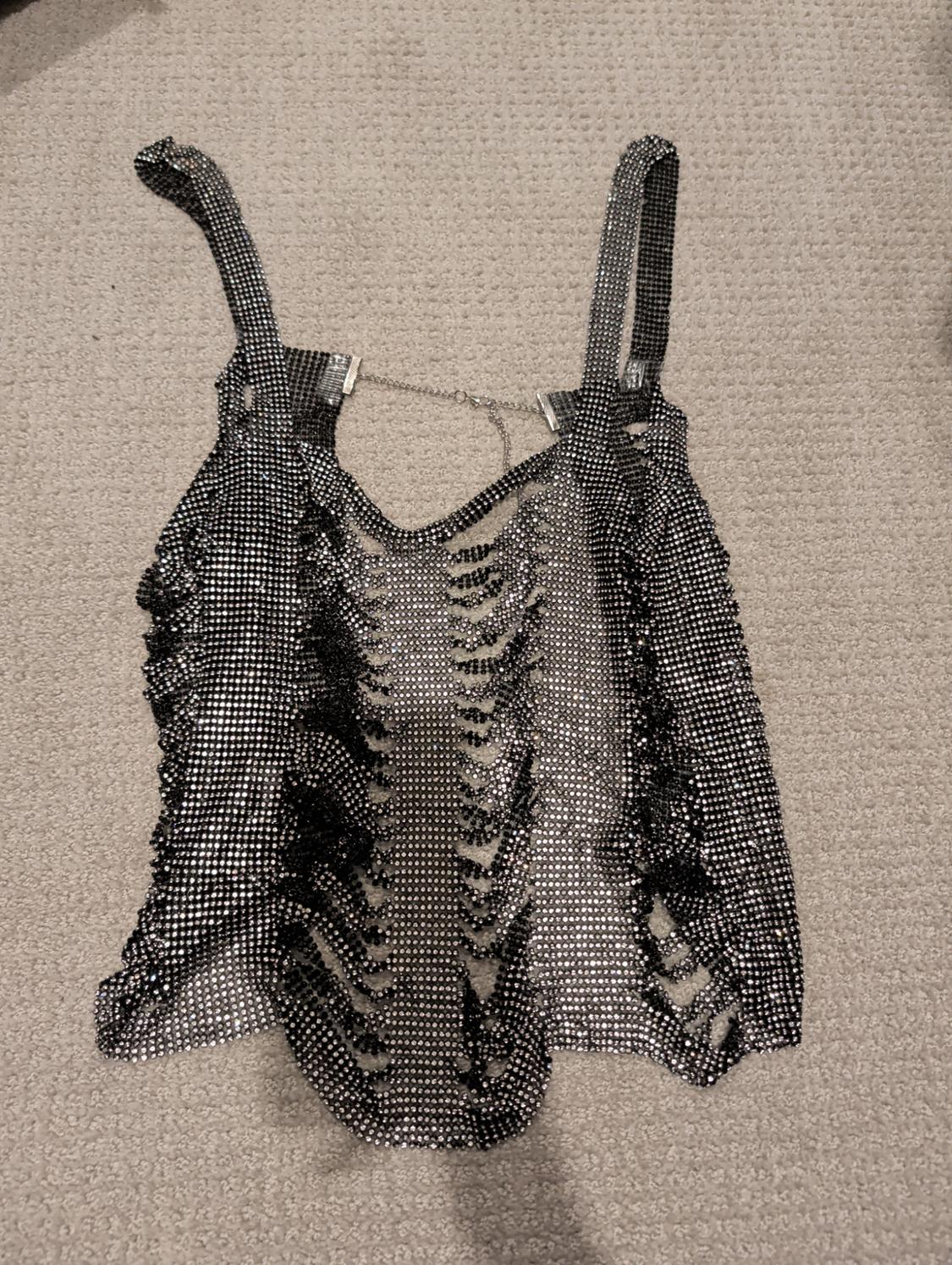 Metallic mesh top with thin straps and cut-out design, on a beige rug.