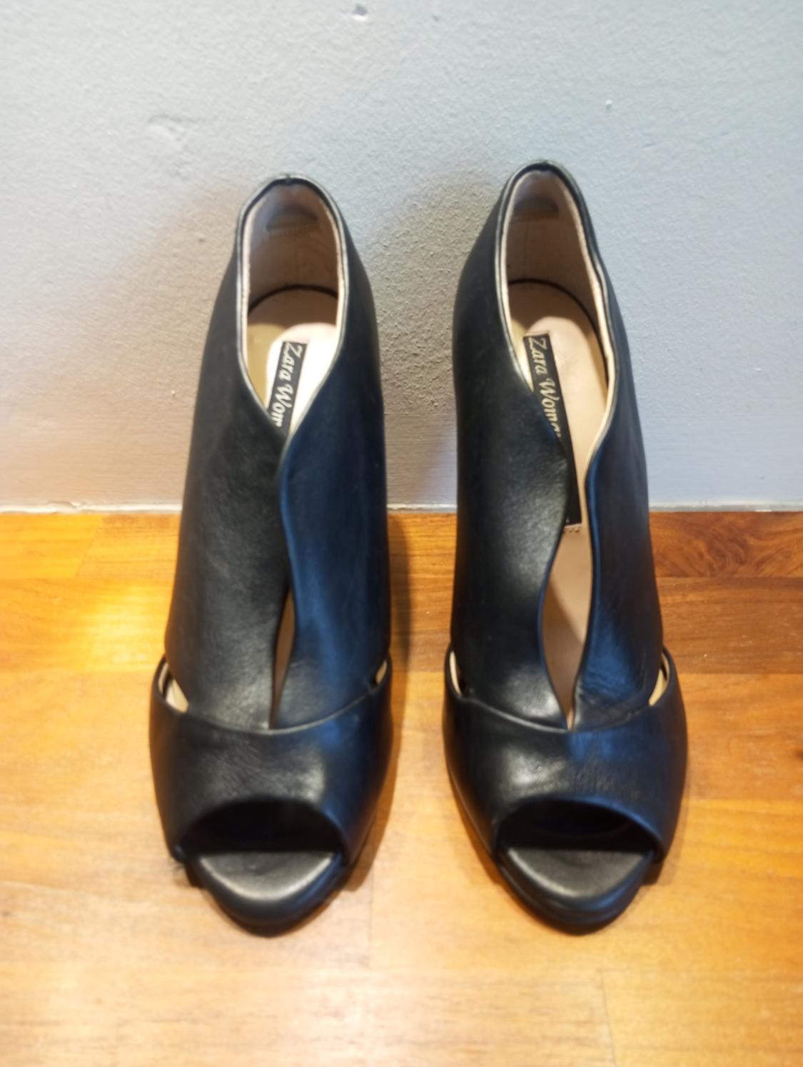 Black high-heeled shoes with an open toe, on a wooden floor. Visible label: "Zara Woman".