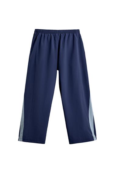 Front view of blue trousers with elasticated waistband and concealed side pockets. Contrasting side stripe detail.