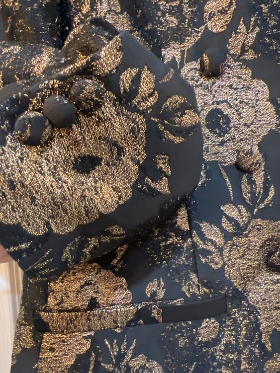 Detail of a black jacket with a shiny gold floral print and covered buttons, creating an elegant and sophisticated style.