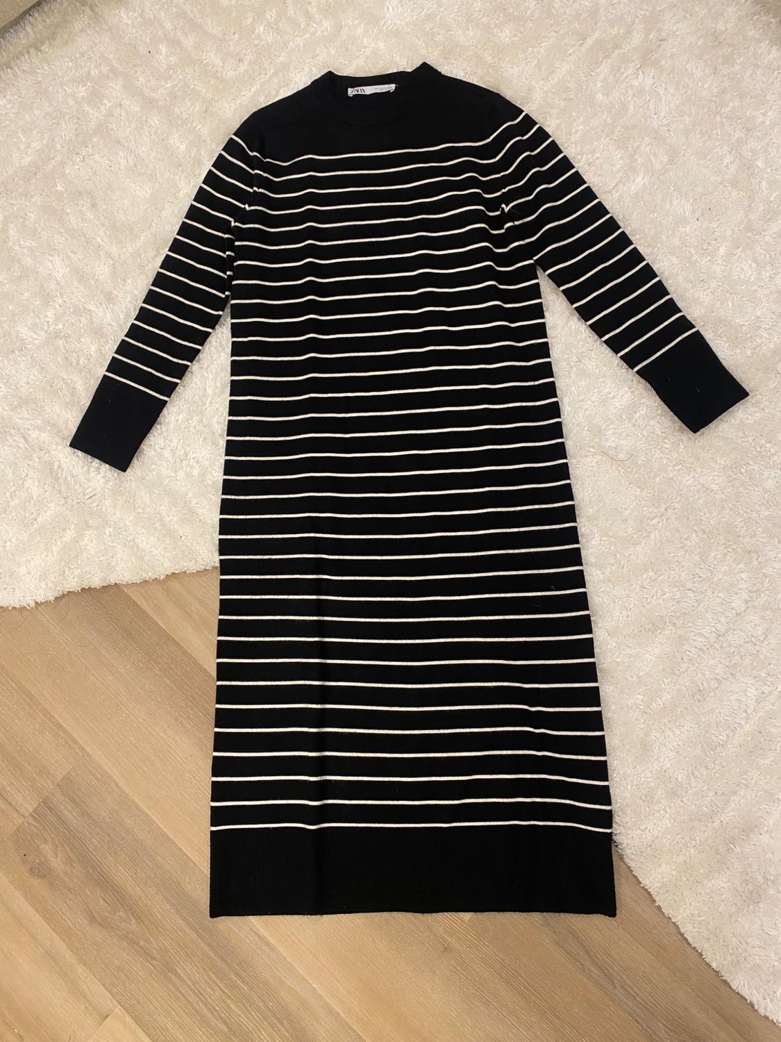Black dress with white stripes on a white rug and light wood floor. Visible tag on the collar.