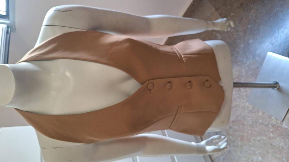 White mannequin with a camel-coloured tailored waistcoat, deep V-neck, and four front buttons, on a metal stand in a studio.