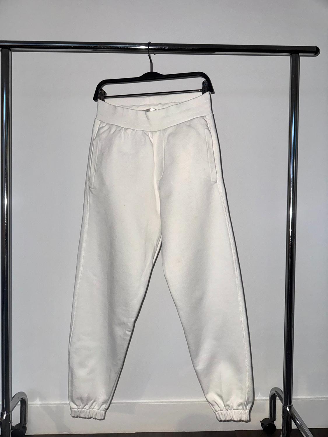 White trousers hanging on a black hanger on a metal stand. White background and dark floor.