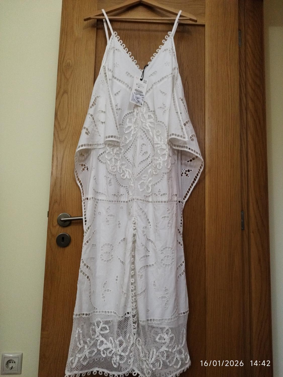 White lace dress hanging on a wooden door. Label visible. Date and time in the bottom right corner: 16/01/2026 14:42.