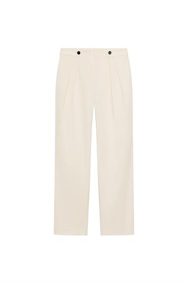 Front view of ecru trousers with pleats, front pockets, faux back pockets, and zip and button fastening.