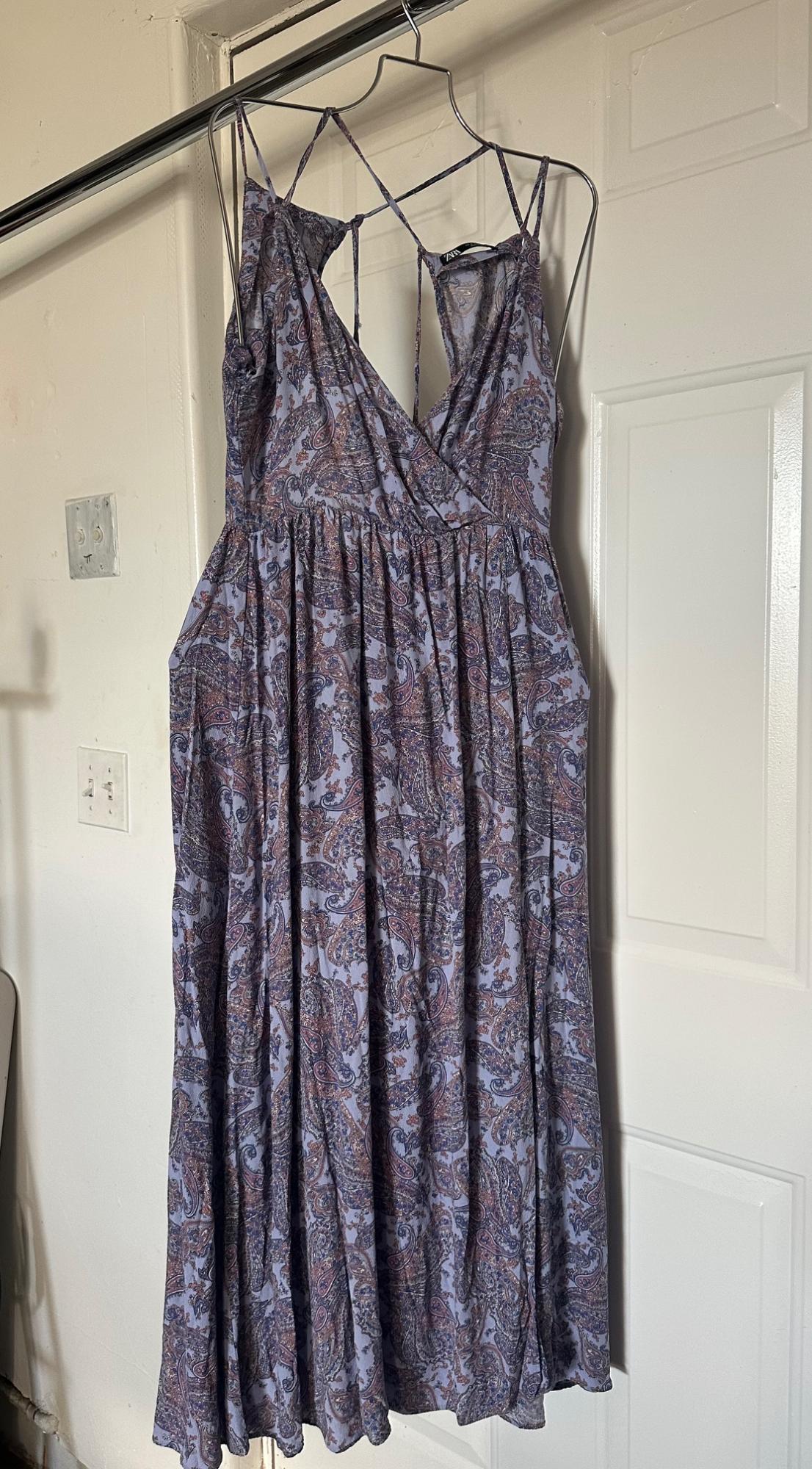 Long dress with paisley print in shades of purple and blue, hanging on a metal hanger in front of a white door.