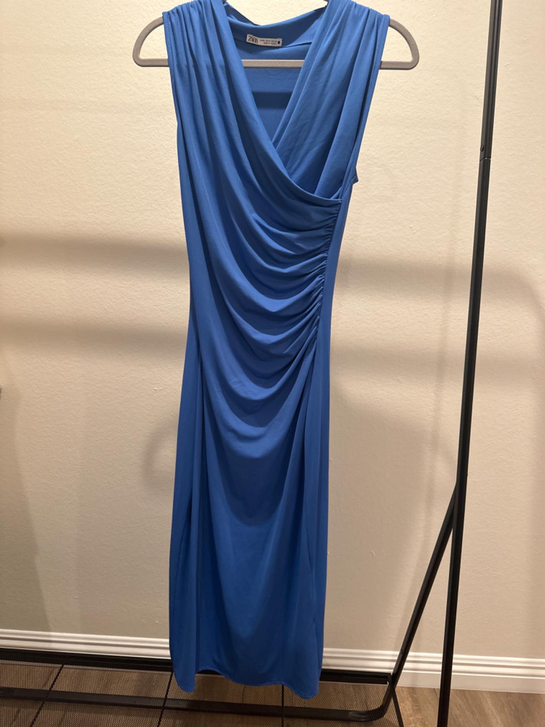 Front view of a sleeveless blue dress with side ruching and a crossover neckline.