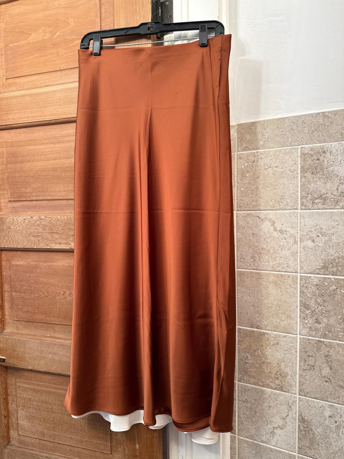 Terracotta long skirt hanging on a black hanger, wooden door background and beige tiled wall.