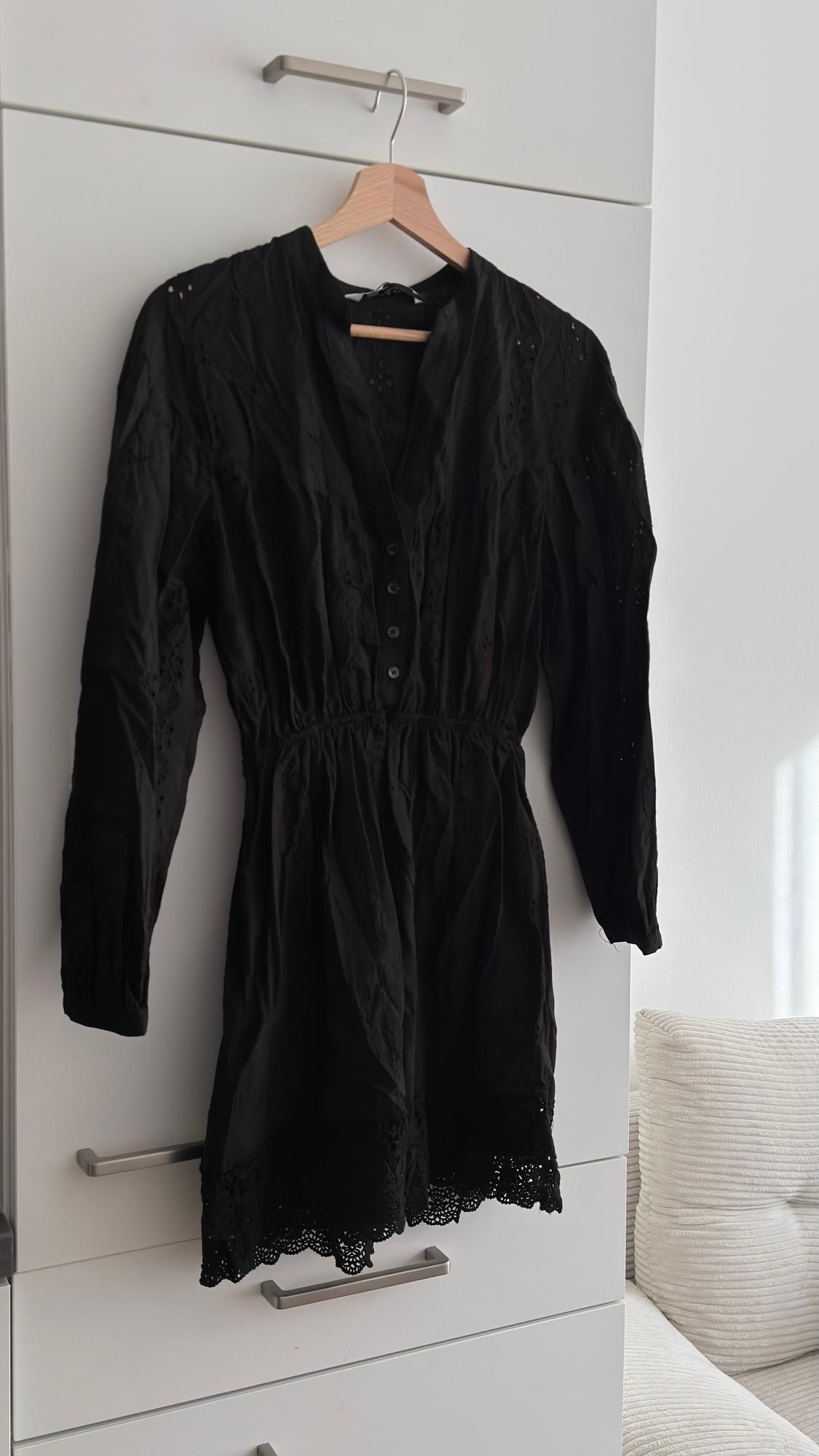 Long-sleeved black dress with buttons and lace details hanging on a wooden hanger over a white wardrobe.
