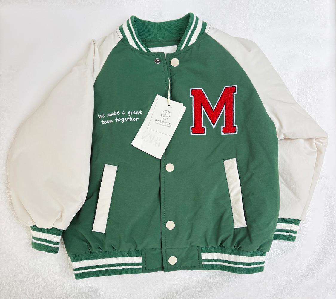 Green and white varsity-style jacket on a white background. Visible text: We make a great team together, M, ZARA.