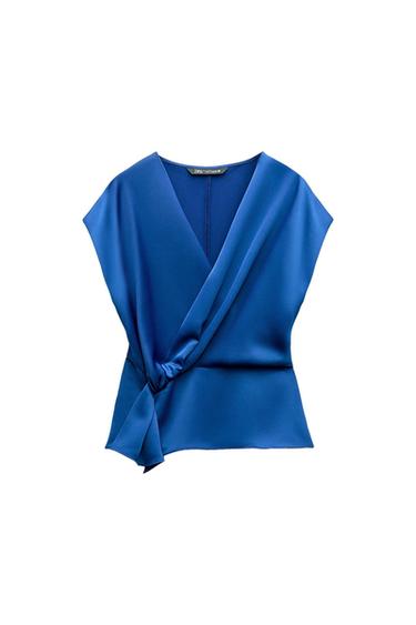 Satin blue sleeveless top with a V-neck and a knot detail at the hem on a white background. Internal label with the text ZARA.